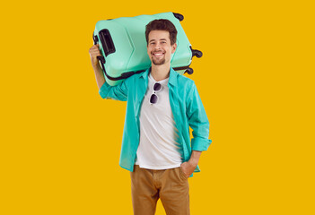 Travel. Portrait of happy young man with suitcase who is going on vacation to warm country. Smiling Caucasian man in summer casual clothes holding suitcase on shoulder isolated on orange background.