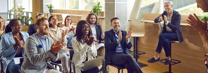 Happy audience applauding speaker for his successful presentation at business meeting or conference. Group of diverse multiethnic people sitting in office, clapping hands and smiling. Banner, header