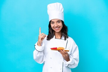 Young hispanic chef woman holding sashimi isolated on blue background pointing up a great idea