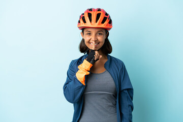 Young cyclist woman isolated on blue background showing a sign of silence gesture putting finger in mouth
