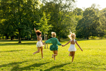 Obraz premium Three happy women in dresses running barefoot in the park at sunset