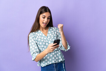 Young caucasian woman isolated on blue background with phone in victory position
