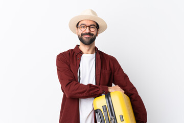 Traveler man man with beard holding a suitcase over isolated white background keeping the arms...