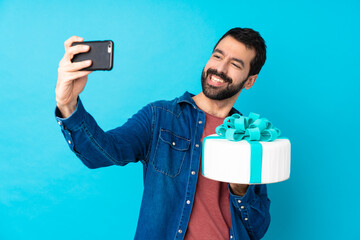Young handsome man with a big cake over isolated blue background making a selfie