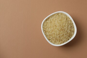 Raw brown rice in bowl on color background