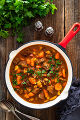 Beef goulash with vegetables in frying pan on wooden table	