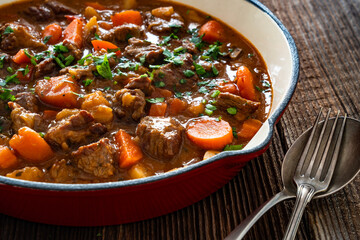 Beef goulash with vegetables in frying pan on wooden table	