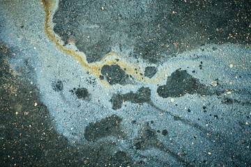 Brilliant oil spill creates a vibrant display on the pavement next to a crowded urban street during a sunny day.