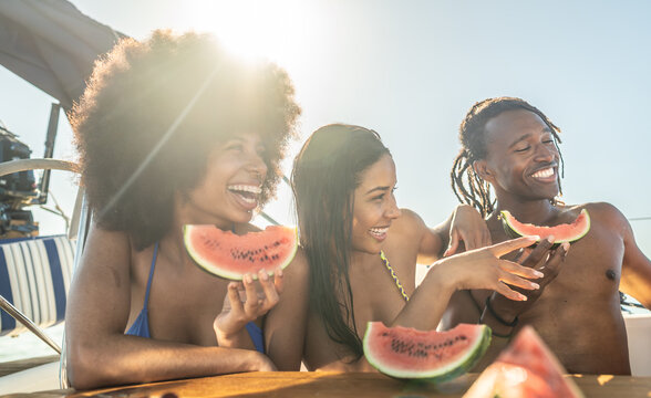 Three young adults laughing and eating watermelon under the sun on a boat. Vibrant summer vibes and joyful friendship.