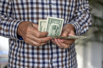 Frontal close-up of a man counting a wad of American Dollar banknotes, in 20 dollar denomination. Cash in hand concept - wages, payment, dividends, investment, austerity, loan or winnings.