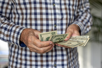 Frontal close-up of a man counting a wad of American Dollar banknotes, in 10 and 20 dollar denominations. Cash in hand concept - wages, payment, dividends, investment, austerity, loan or winnings.