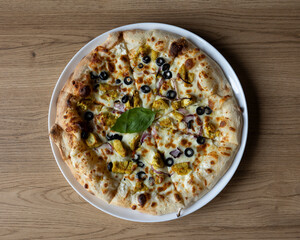 Overhead view of a chicken pizza with olives and basil on white plate