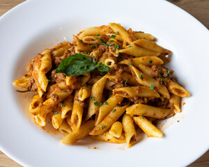 Close up of penne pasta with meat sauce and basil in a white bowl dish
