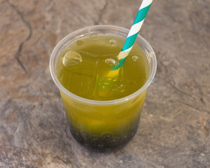 A clear plastic cup filled with a green drink and a striped straw in it