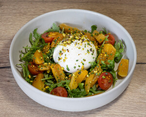 Close up of a burrata salad with tomatoes and orange segments in a bowl