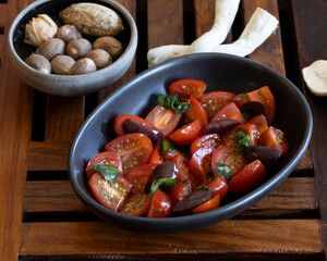 A bowl of tomato salad with basil and olives next to other ingredients