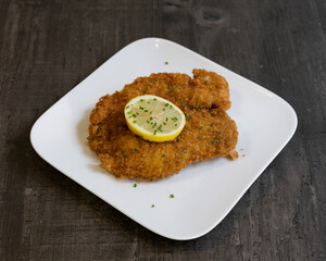 Breaded schnitzel with lemon slice on white plate for traditional European meal visuals