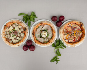 Three assorted gourmet pizzas with prosciutto, burrata, grilled vegetables and herbs for Italian food visuals