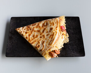 Savory crepe filled with sausage and cheese on a black rectangular plate