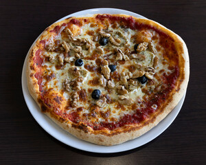 Close up shot of a pizza with walnuts and olives on a white plate top