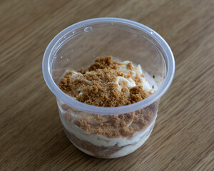 Dessert in a clear plastic cup with layers of cream and cookie crumbs