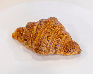 A single golden brown croissant on a plain white surface close up view