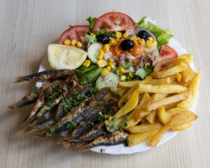 Grilled sardines with French fries and fresh vegetables for Mediterranean seafood meal visuals