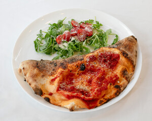 Close up of accalzone with tomato sauce and a side salad on white plate