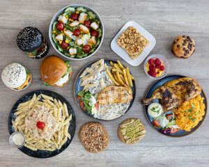 Large variety of Western meals including burgers, pasta, chicken, fries, salads and desserts on shared table setup