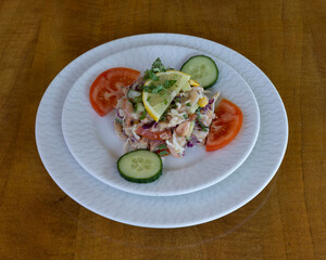 Cold tuna salad with corn, cucumber and tomato slices garnished with lemon and herbs for appetizer visuals