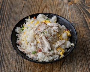 Chicken fried rice served in a black bowl on a wooden textured table