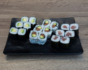 Assorted sushi rolls on a black plate with wooden background visible