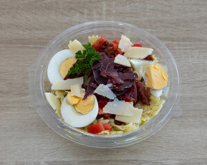 Overhead view of a pasta salad with eggs and meat in a plastic bowl