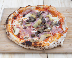 Overhead view of a pizza with ham artichokes and mushrooms on a board