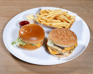 Two burgers with fries and sauces on a white plate on a wooden table