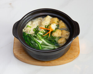A bowl of wonton soup with vegetables on a wooden serving board dish