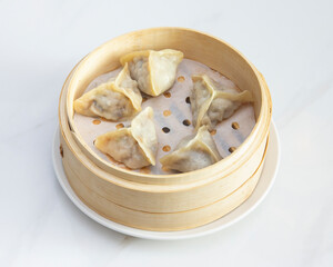 Steamed dumplings in a bamboo steamer basket on a white background plate