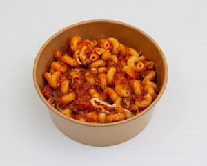 Cavatappi pasta with meat sauce in a brown paper bowl on white surface