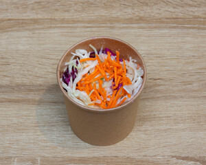 Top view of coleslaw in a brown paper cup on a wooden surface top