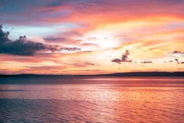 Serene sunset over calm sea with soft pink clouds and orange glow lighting up the peaceful sky.