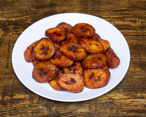 A plate full of fried plantains on a wooden table close up view shot © Studio Just M