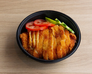 A black bowl filled with sliced fried chicken and sliced vegetables