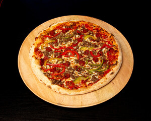 Overhead shot of a pizza with meat and peppers on a wooden platter
