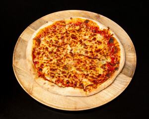 Top view of a cheese pizza on a wooden plate against a black background