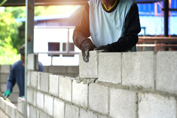 masonry worker make concrete wall by cement block and plaster at construction site 

