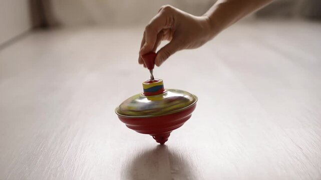 Hand launching a colorful spinning top toy on a wooden floor in a softly lit room

