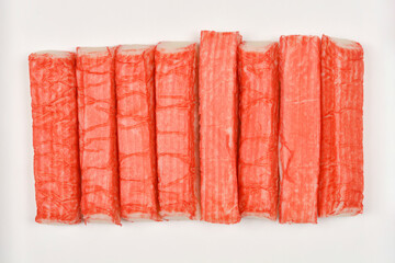 A top-down view of several surimi sticks neatly arranged in a row against a plain white background,...
