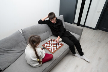 On a chilly afternoon, a captivating chess match unfolds in a cozy living room, where a young boy and girl are deeply focused on their game