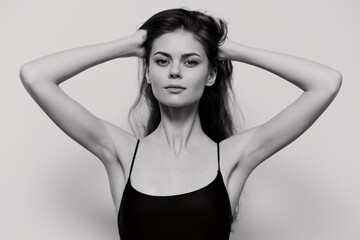 Fototapeta premium Confident young woman in black swimsuit, posing with hands in hair against a neutral grey background. Emphasizing beauty and self-expression concepts.
