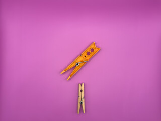 Modern orange plastic clothes peg versus old wooden brown clothes peg centered on purple background...
